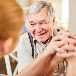 Senior man smiling, holding hands with health care provider