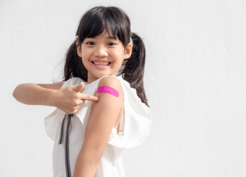 girl smiling and pointing to the bandaid after getting a vaccine