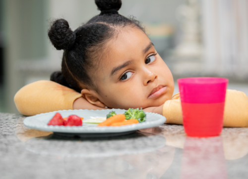 little girl with plate of food that she doesn't want to eat