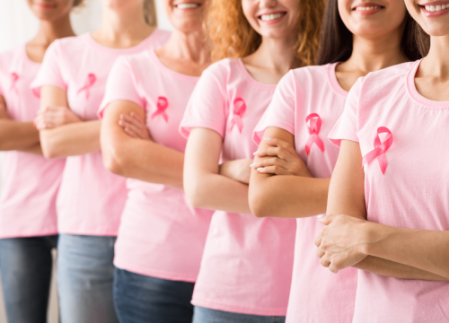 women standing in a line wearing breast cancer ribbons on their shirts