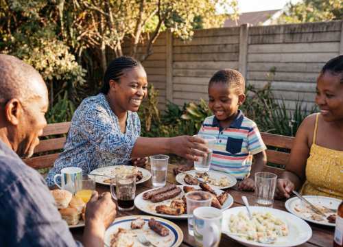 a woman seated at a table with her family, enjoying barbeque food.