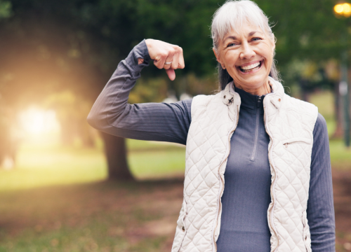 senior woman smiling outside, holding her arm up in strength
