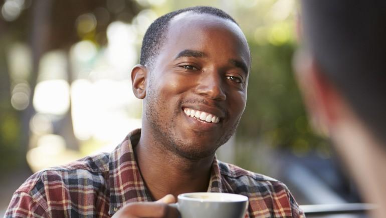 man smiling and drinking coffee outdoors