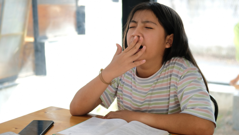 teen who is tired and yawning while reading a book