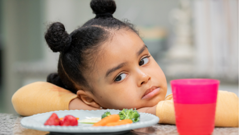 little girl resisting eating a plate of food