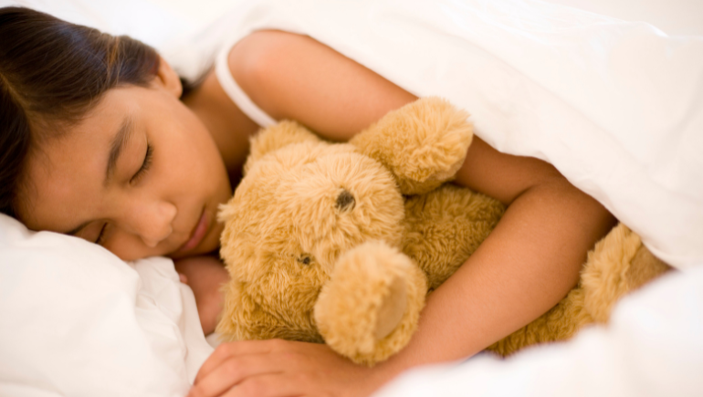 child sleeping in bed with teddy bear