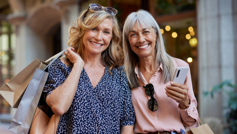 two middle aged women smiling holding shopping bags together