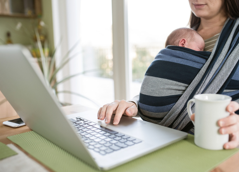 New mother sitting at laptop with sleeping baby 
