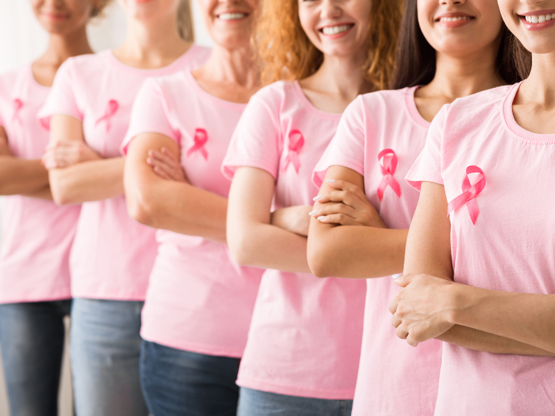 women standing in a line wearing breast cancer ribbons on their shirts
