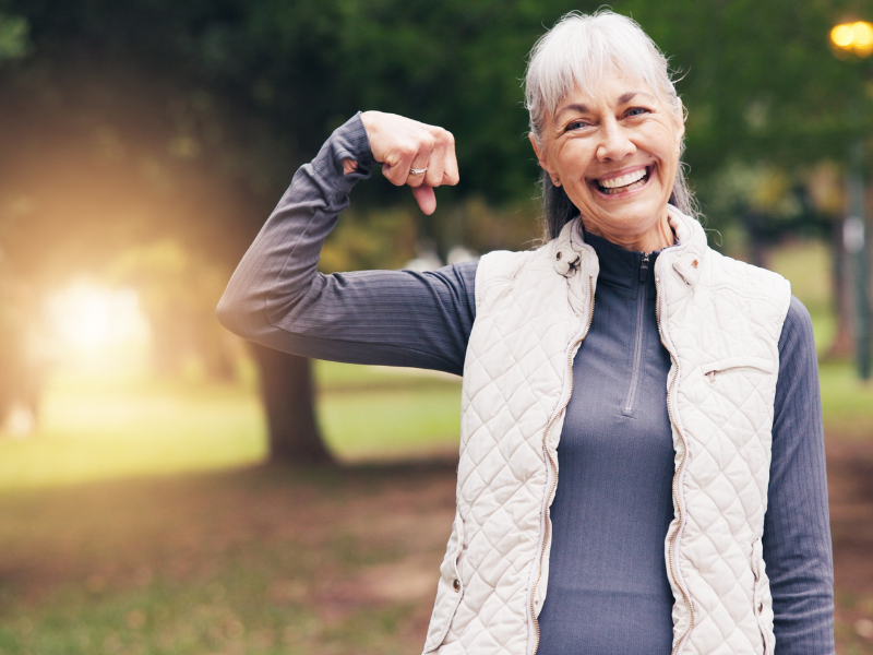 senior woman smiling outside, holding her arm up in strength